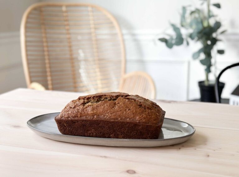 Banana Bread on Small Platter on a wood table with a chair and a plant in the background 